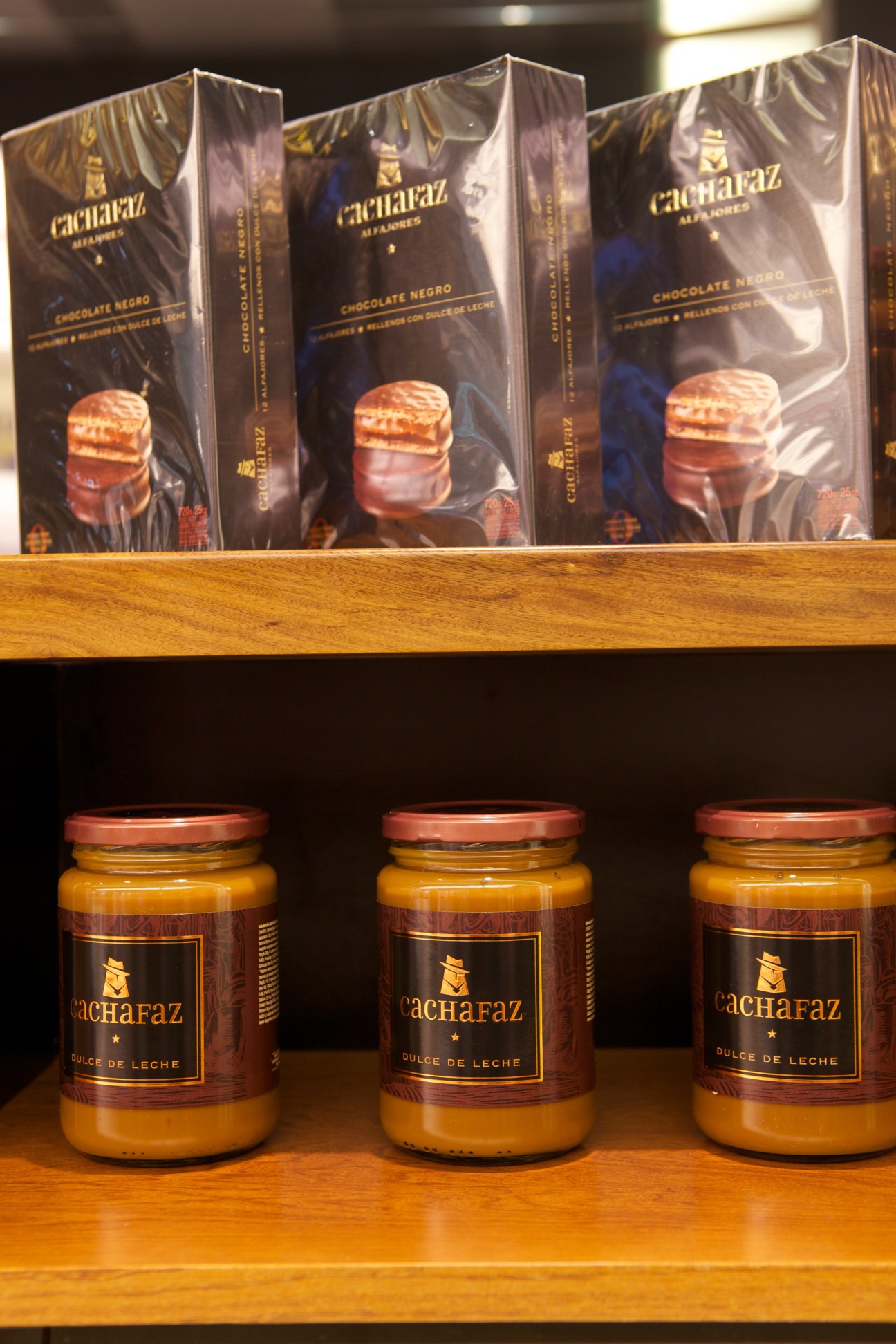Cachafaz alfajore packages and dulce de leche jars displayed on wooden shelves.