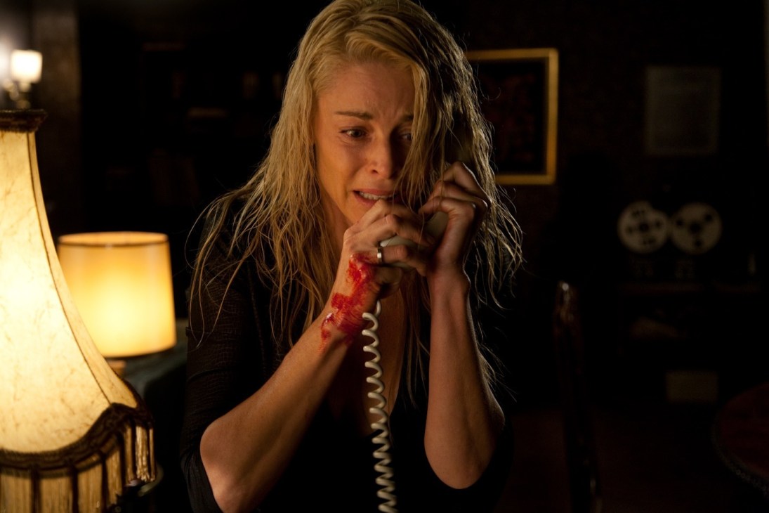 Woman with wet hair holding a bloody phone cord, looking distressed in a dimly lit room.