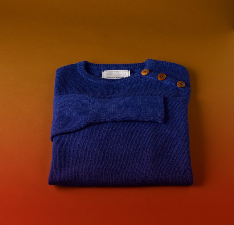 Blue alpaca knit jumper with orange buttons and stripe detail on orange background.