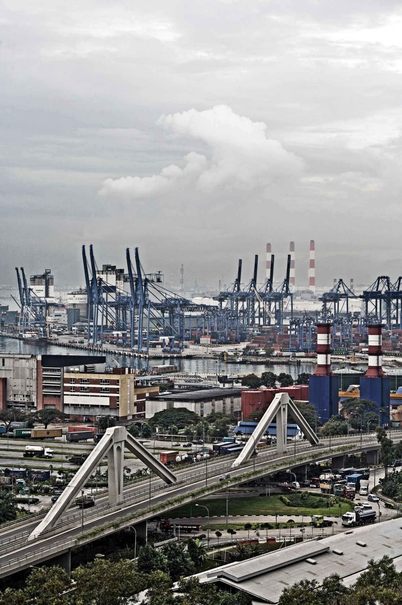 Aerial view of Jurong Island's industrial port with container cranes, stacked cargo containers, and a white bridge crossing over reclaimed land.