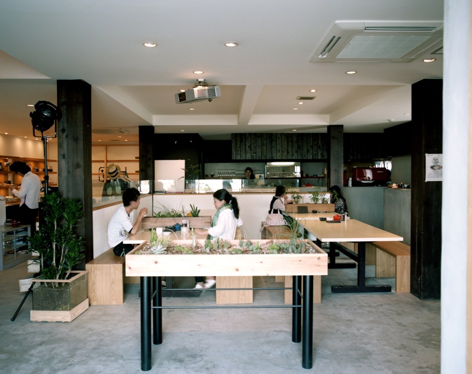 Interior of Good Neighbors café with wooden tables, potted plants, and customers dining in a modern minimalist space.