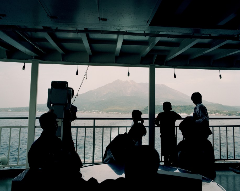 Silhouetted passengers aboard a ferry viewing Sakurajima volcano across the water.