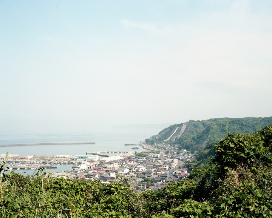 Aerial view of Kanoya fishing port with coastal town, bay waters, and forested hills.