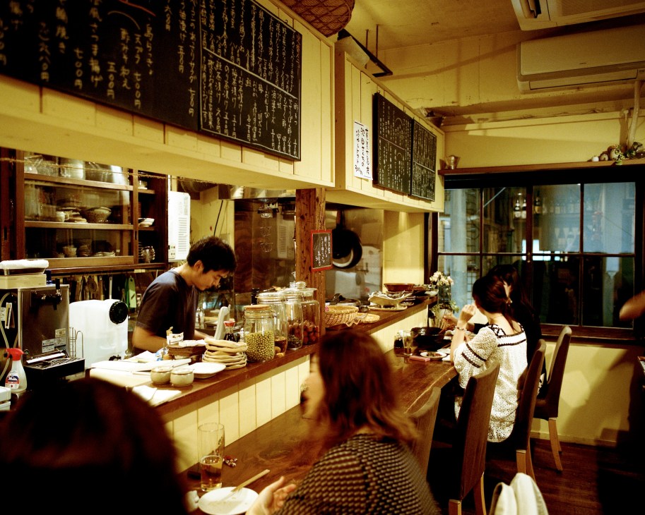 Chef Hideki Muraoka works behind the counter at Daidai restaurant in Kagoshima with warm lighting and Japanese menu boards on the wall.