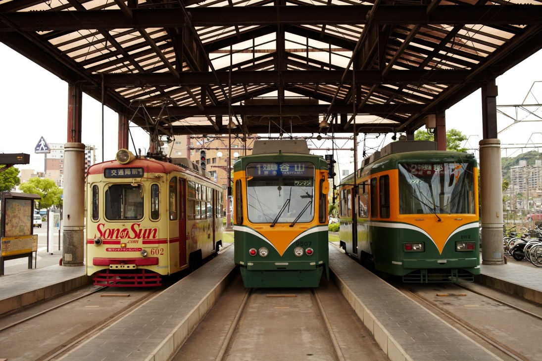 Three vintage trams parked under a metal canopy at Kagoshima Central station.