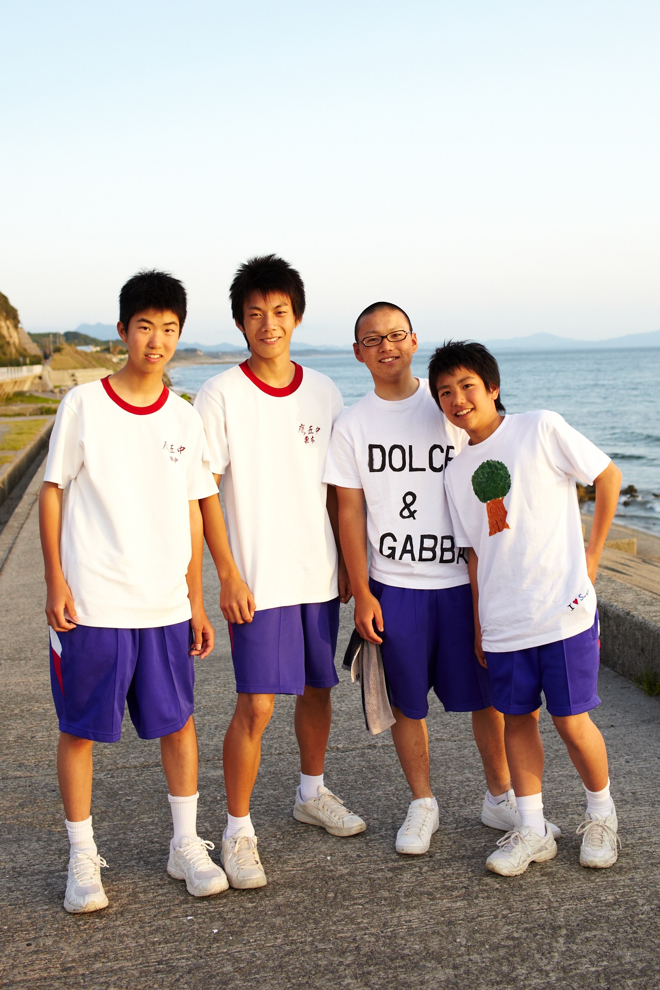 Four high school students standing on a coastal path with the sea behind them.