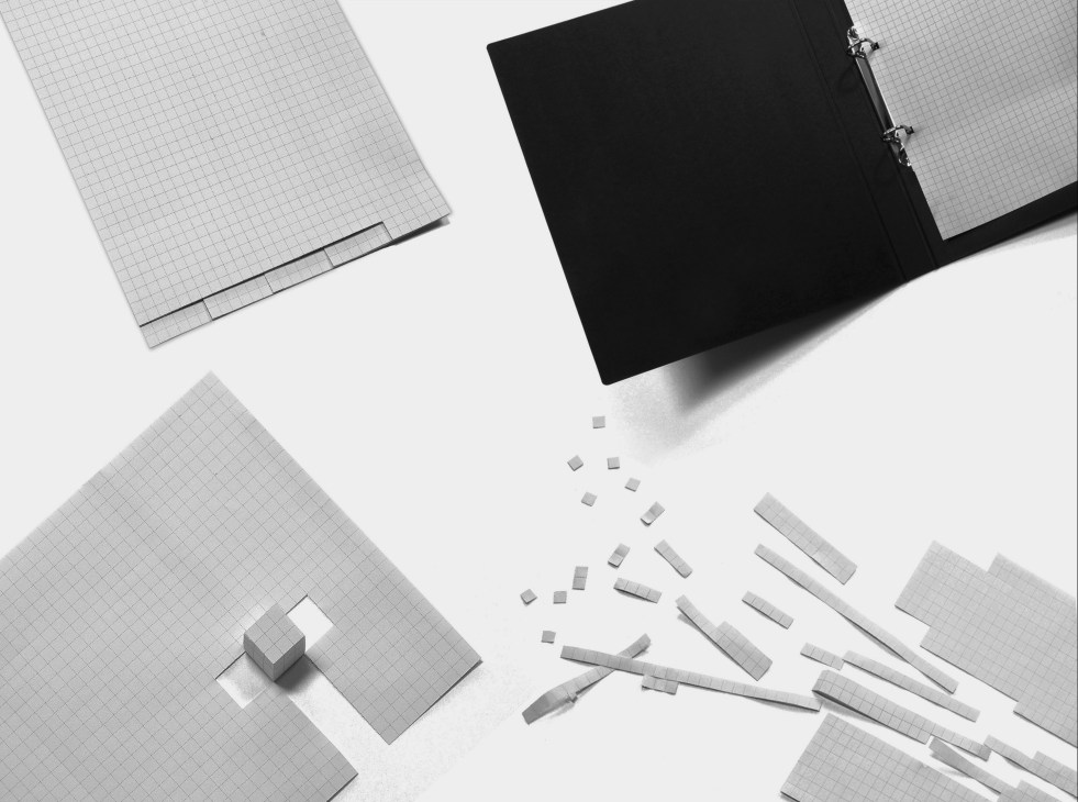 Grid-patterned notebooks, black binder, and perforated paper strips arranged on white surface.