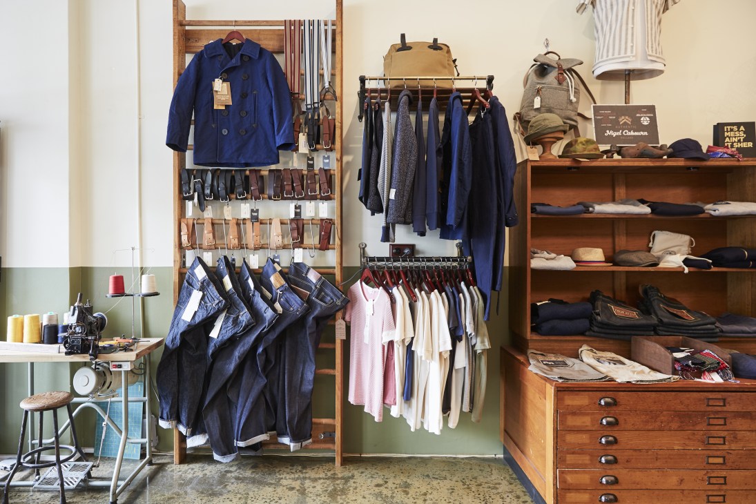 Interior of Pickings and Parry boutique displaying vintage workwear clothing on wooden racks and shelves.