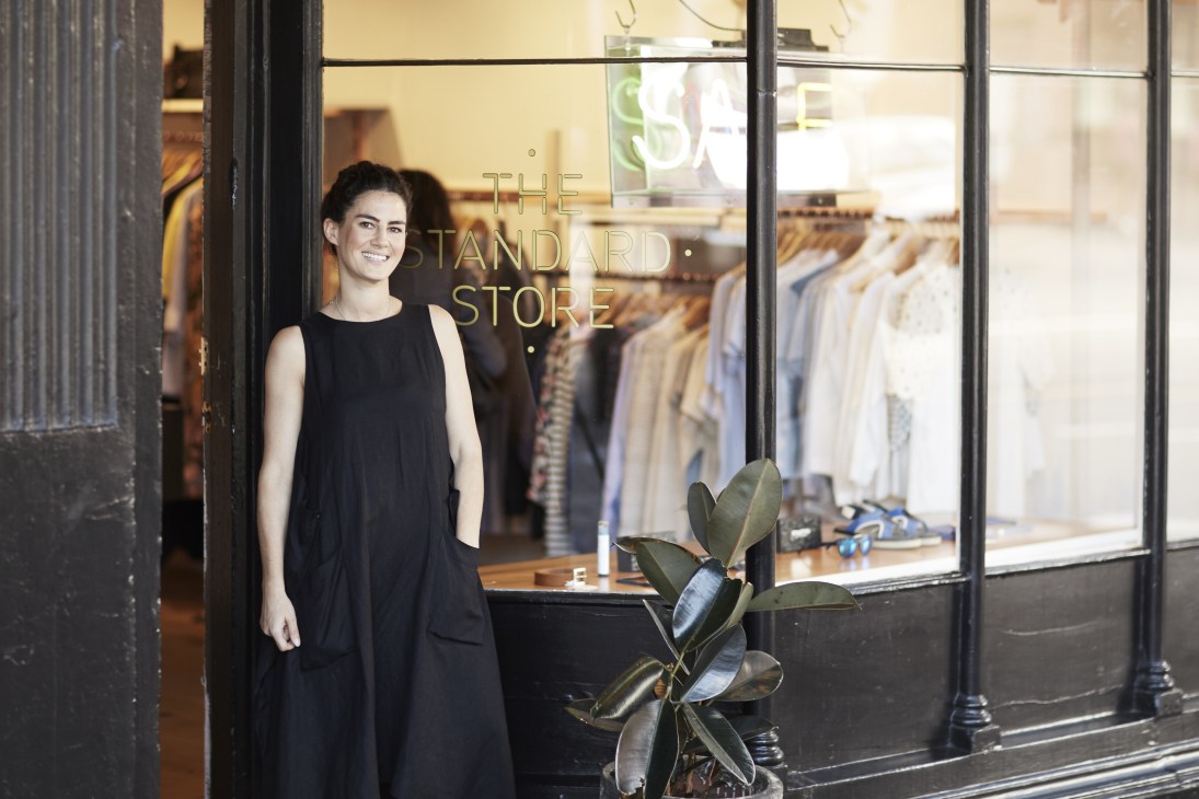 Jacqueline Haywood, owner of The Standard Store, stands in the storefront wearing a black sleeveless dress.