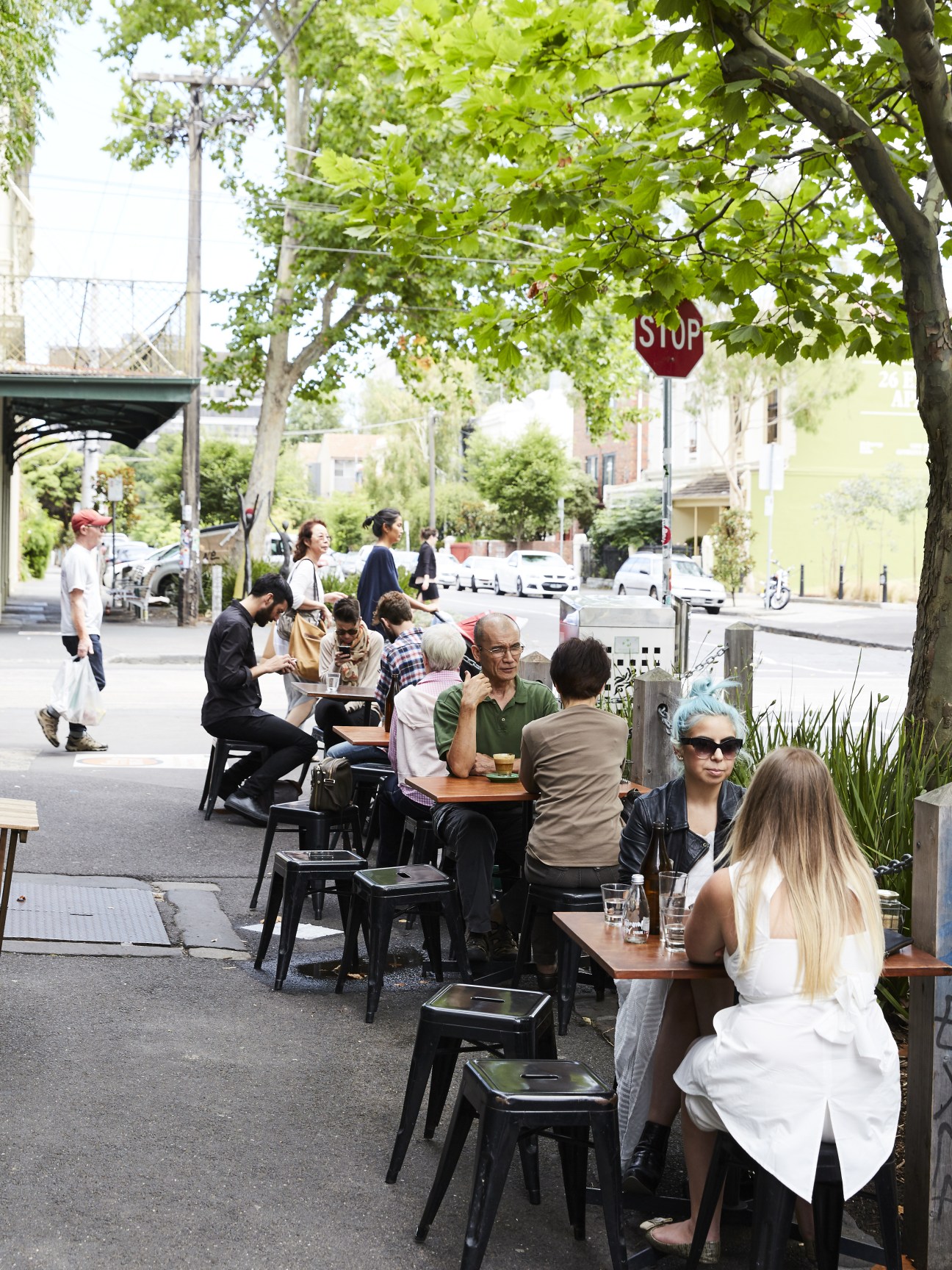 Outdoor café seating on Gertrude Street with diners at wooden tables under shade trees.