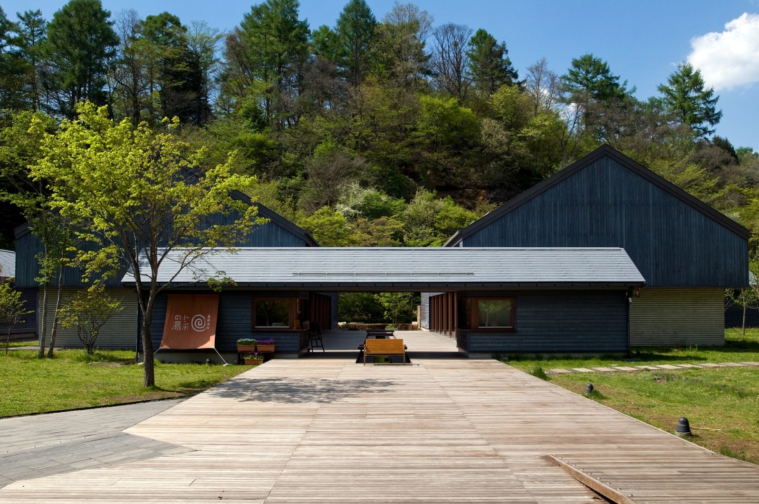 Modern black and white residential building with wooden deck surrounded by lush green forest.