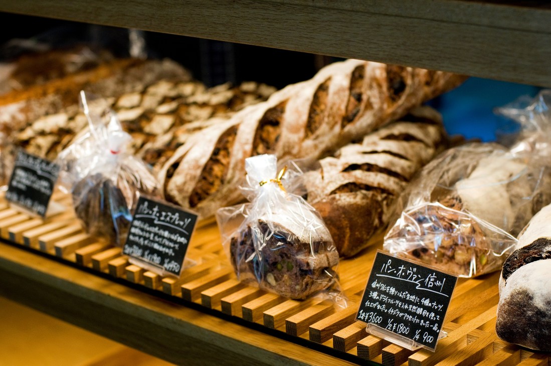 Artisanal breads and pastries displayed in a bakery window with Japanese price labels.