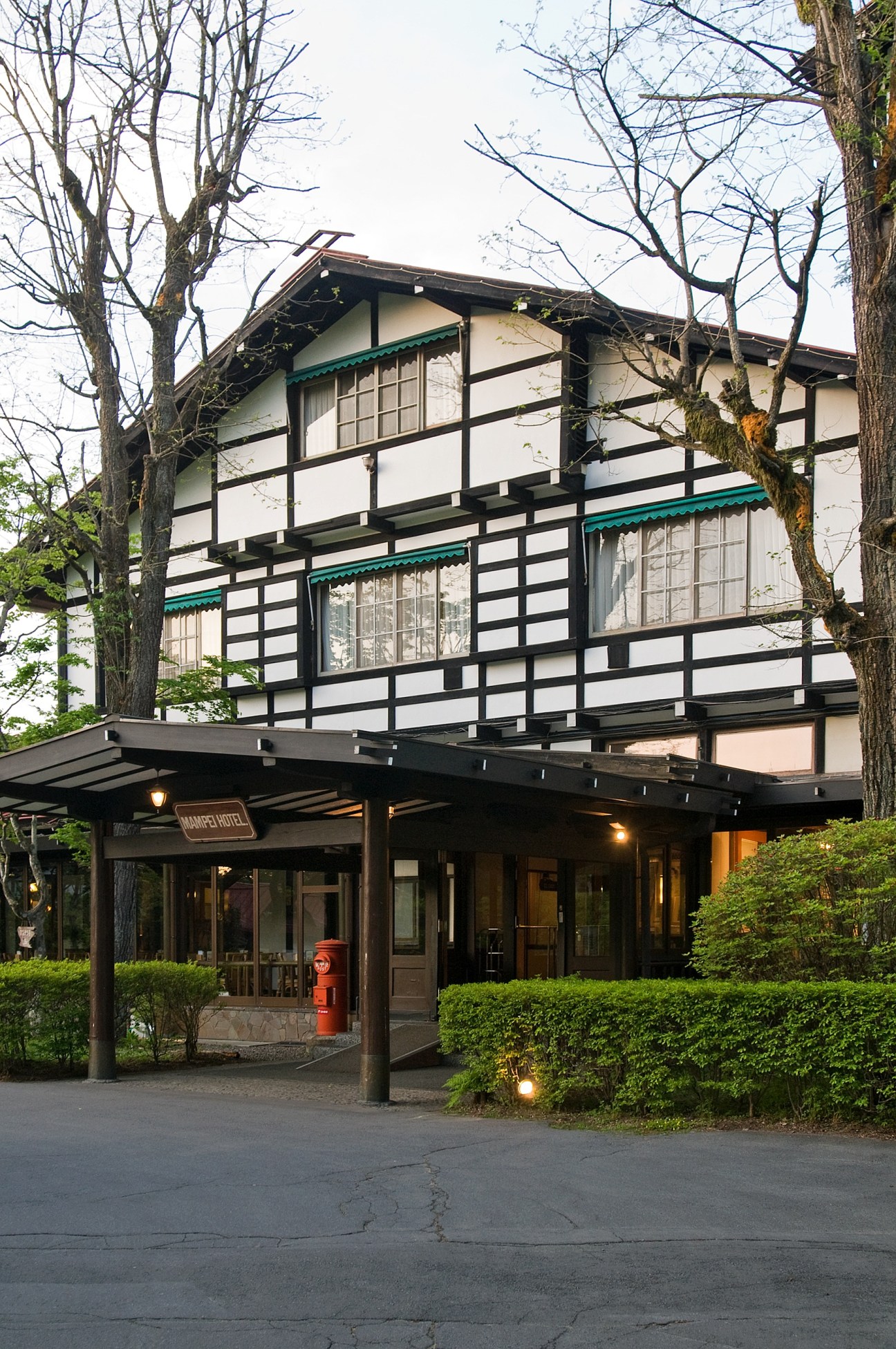 Historic Japanese building with half-timbered facade and green awnings, surrounded by tall bare trees.