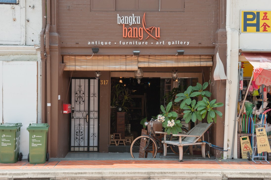 Bangku Bangku antique furniture and art gallery storefront in Katong with brown shophouse facade and vintage bicycle outside.