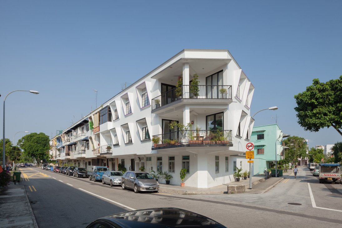 White modernist apartment building with balconies on a Katong street corner, with parked cars and green building visible.