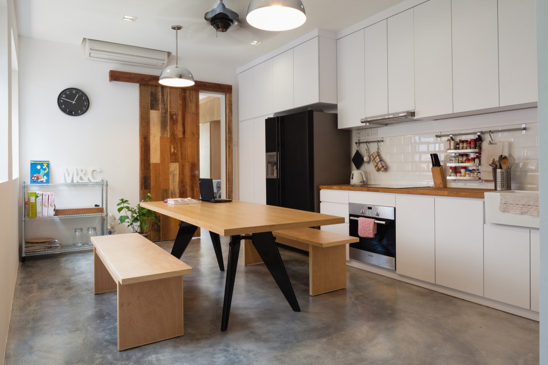 Modern kitchen and dining area with wooden table, white cabinetry, and black appliances in Tan Ngiap Heng's house.