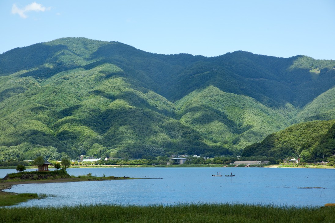 Lake Kawaguchi surrounded by lush green mountains with traditional Japanese buildings visible on the far shore.