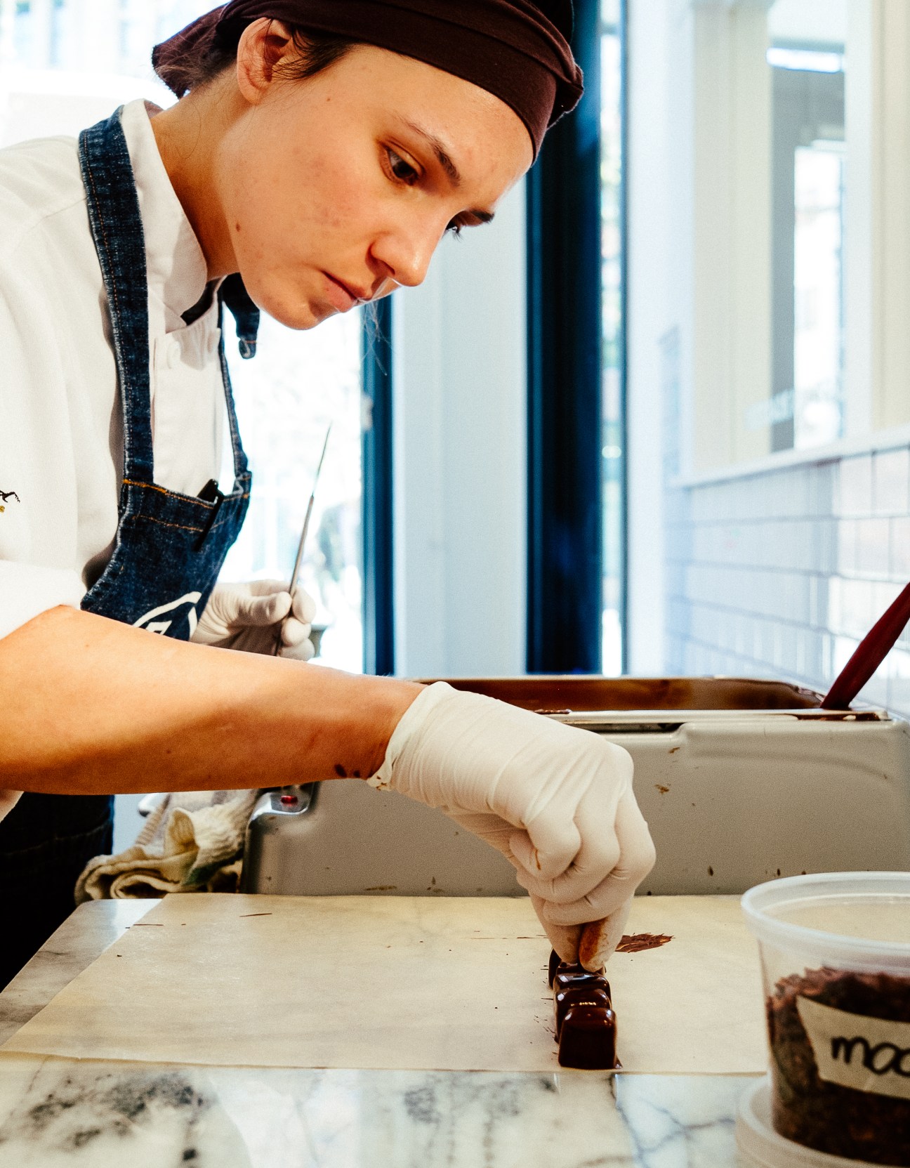 A chocolatier in a denim apron works with melted chocolate on parchment paper in East Van Roasters' chocolate lab.