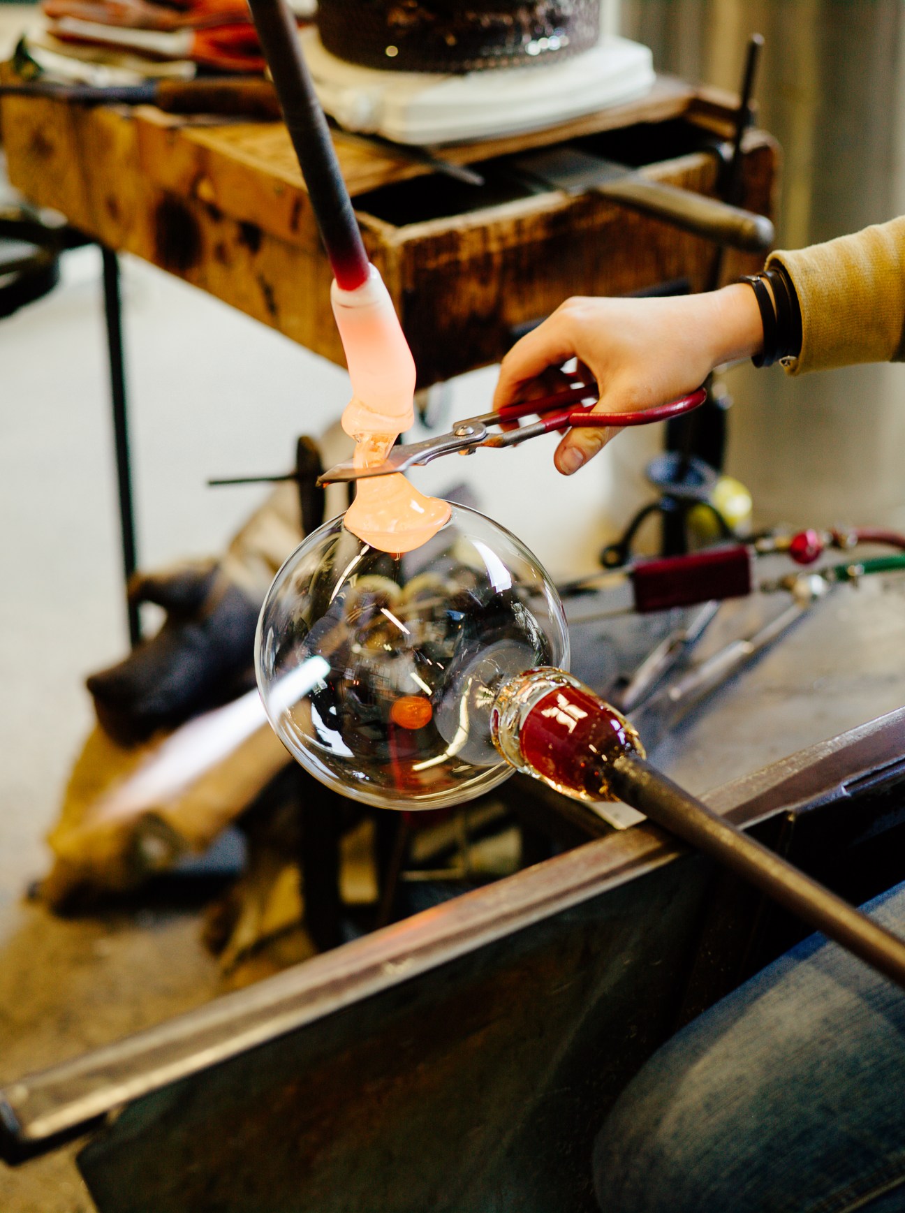 Hands crafting a Bocci glass lighting fixture using tools in a workshop studio.