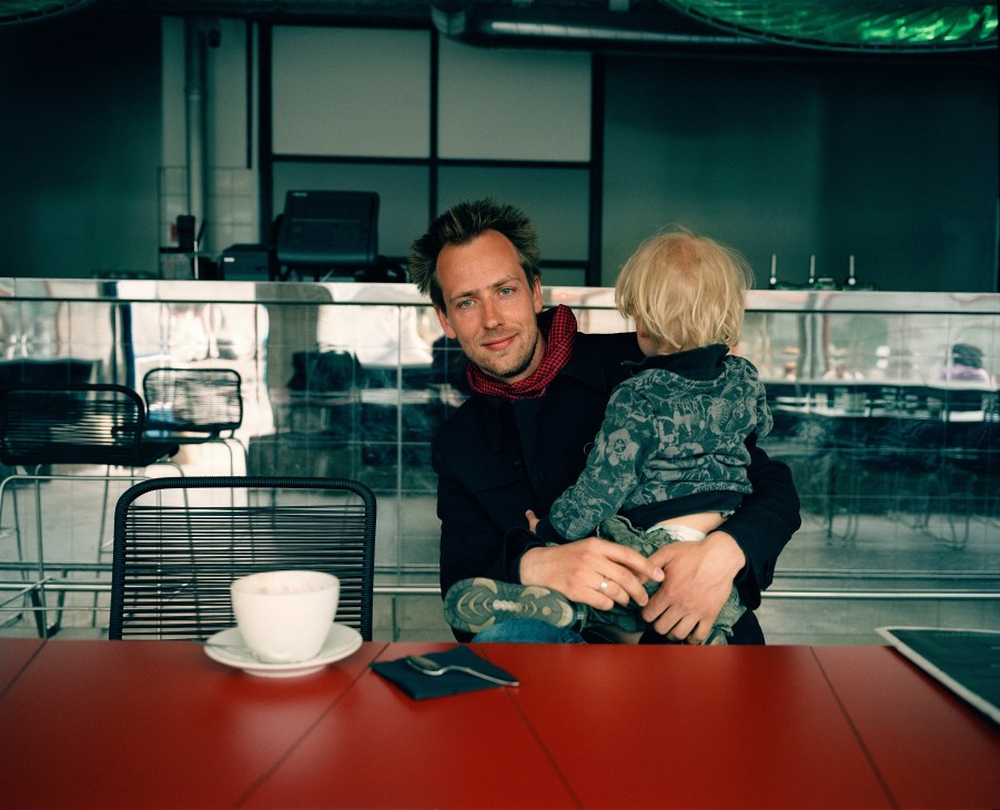 Man holding a young child at a table in a modern café with floor-to-ceiling windows overlooking a city.