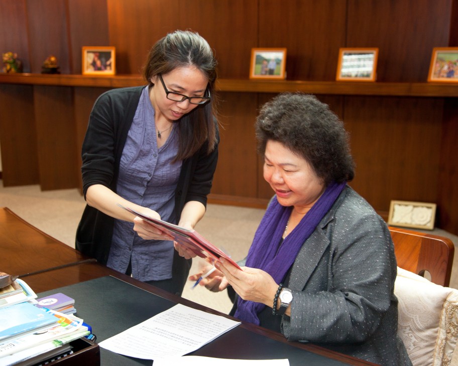 Mayor Chu Chen sits at a desk reviewing documents with a staff member in a wood-paneled office.