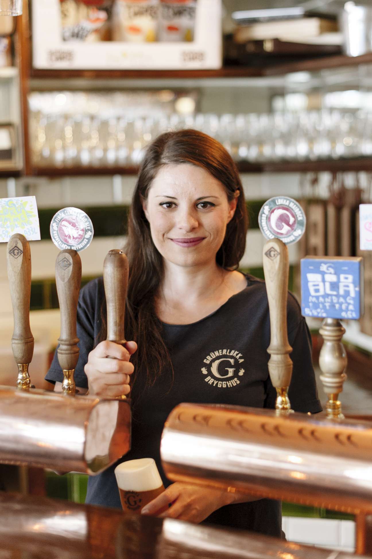 Woman behind a bar at Grünerløkka Brygghus microbrewery in Oslo, holding beer tap handles.
