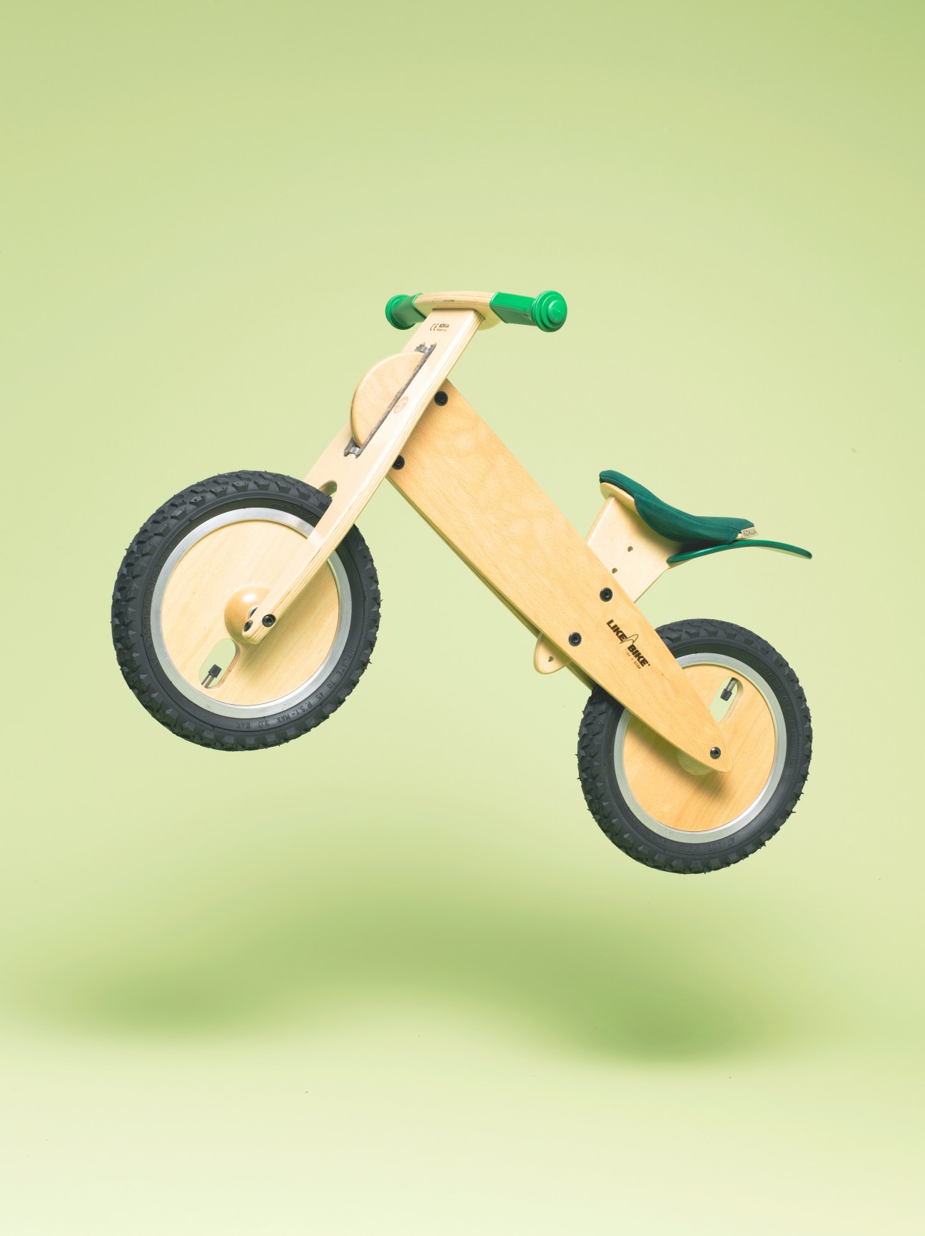LIKEaBIKE wooden balance bike with green handles and seat against a pale green background.