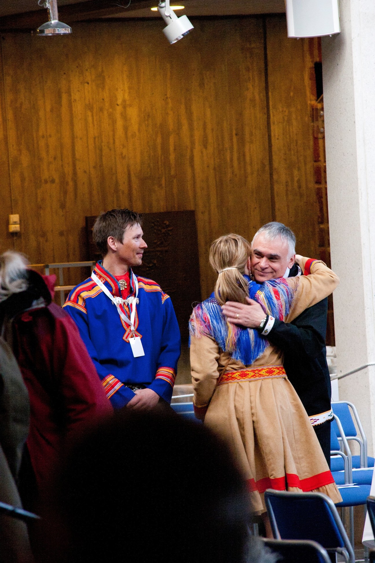Sami delegation members in traditional dress greet a summit participant indoors.