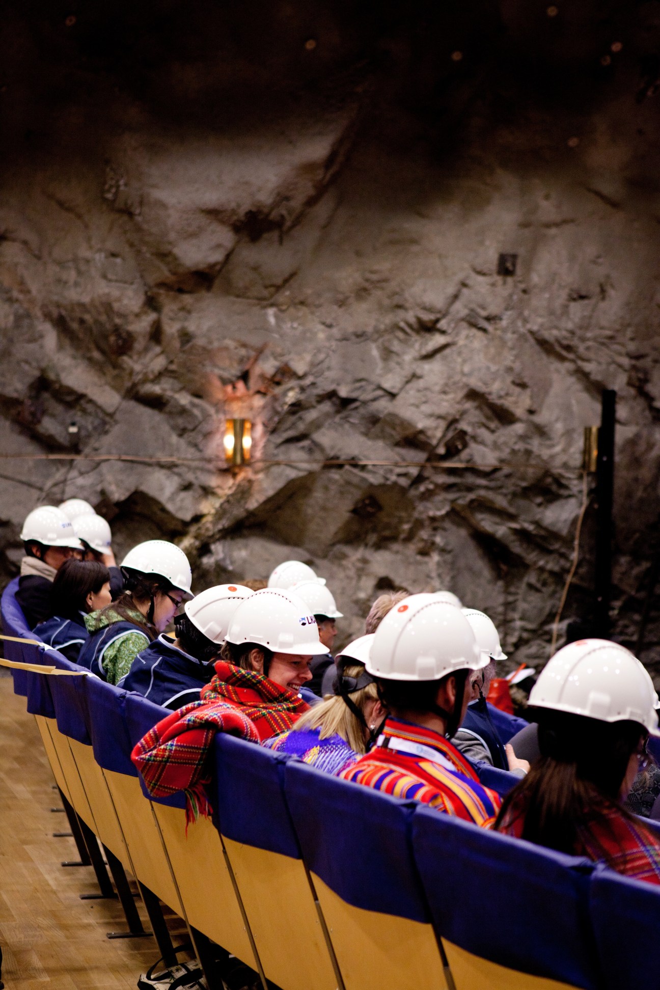 Summit delegates wearing white hard hats sit in a yellow boat touring deep underground within a mine cavern.