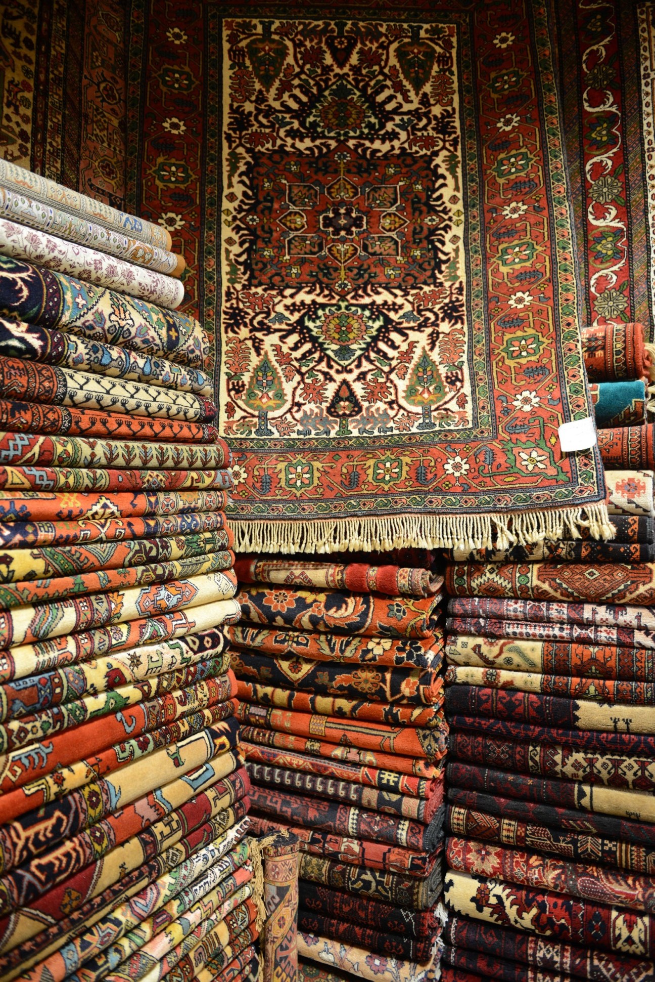 Rolled Persian carpets stacked in colorful piles at Tehran's carpet bazaar display intricate traditional patterns and designs.