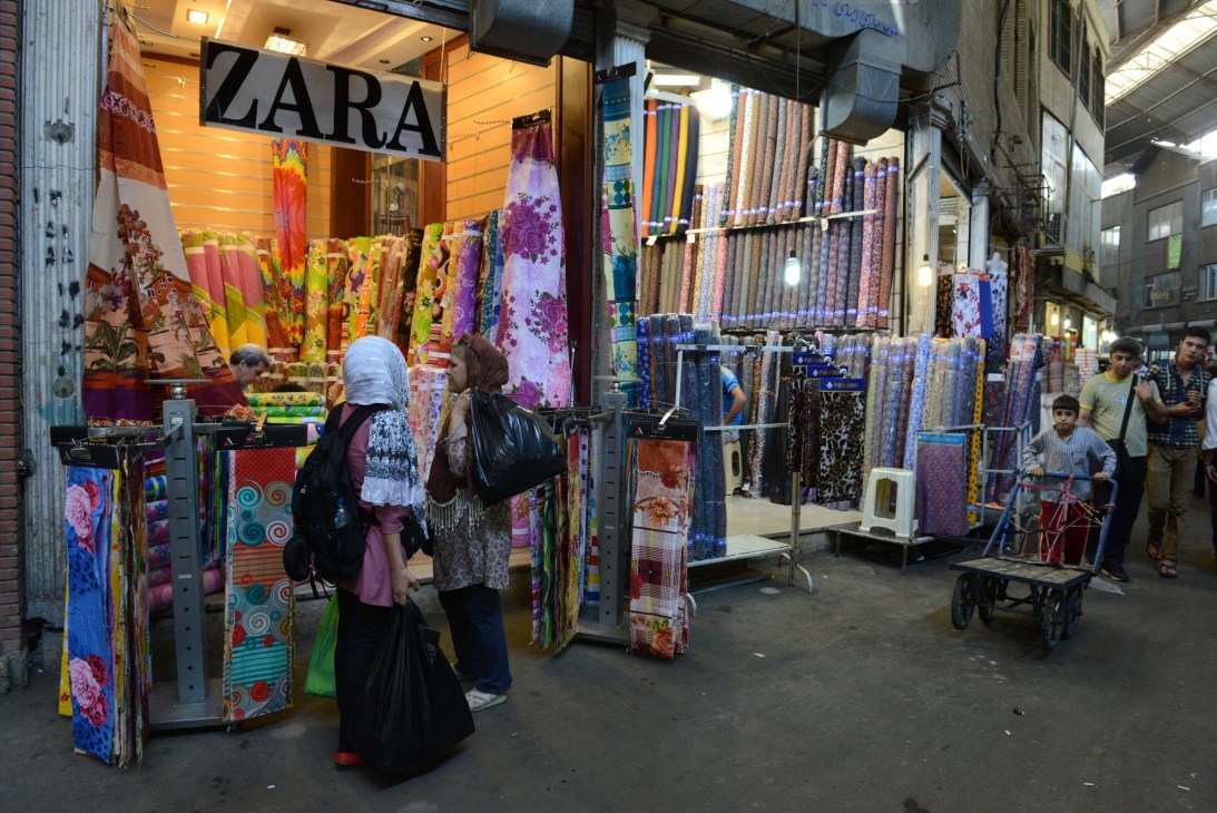 A storefront with a Zara sign displaying colorful fabrics and textiles in Tehran's Grand Bazaar.