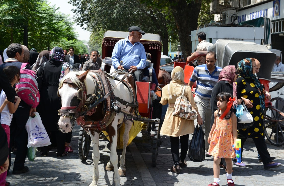 People wait outside the Grand Bazaar as a man sits in a horse-drawn carriage with decorative red panels.