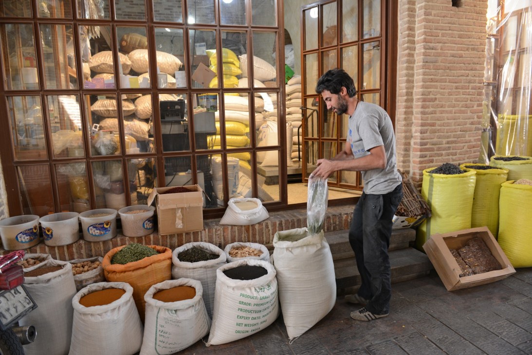 A man puts herbs into a plastic bag outside a spices shop with sacks of colorful spices displayed.