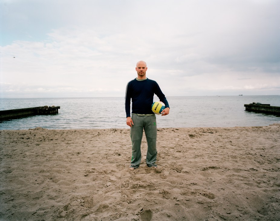 Man holding a volleyball stands on a beach by the sea in Klampenborg, Copenhagen.