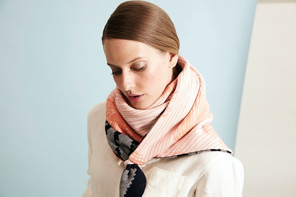 Woman wearing a reversible scarf with digital patterns in coral and cream tones.