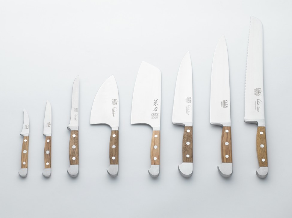 A lineup of eight Güde kitchen knives with wooden handles arranged in order of increasing size against a white background.