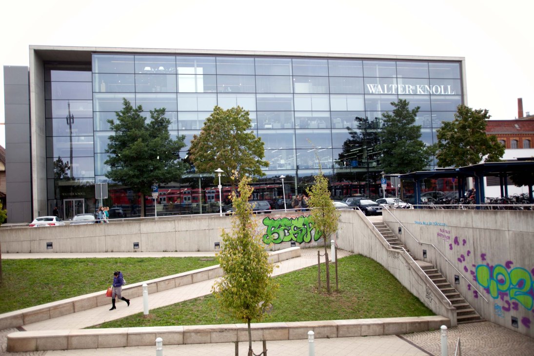 Modern glass-fronted Walter Knoll building with signage, surrounded by landscaped plaza with trees and concrete elements.