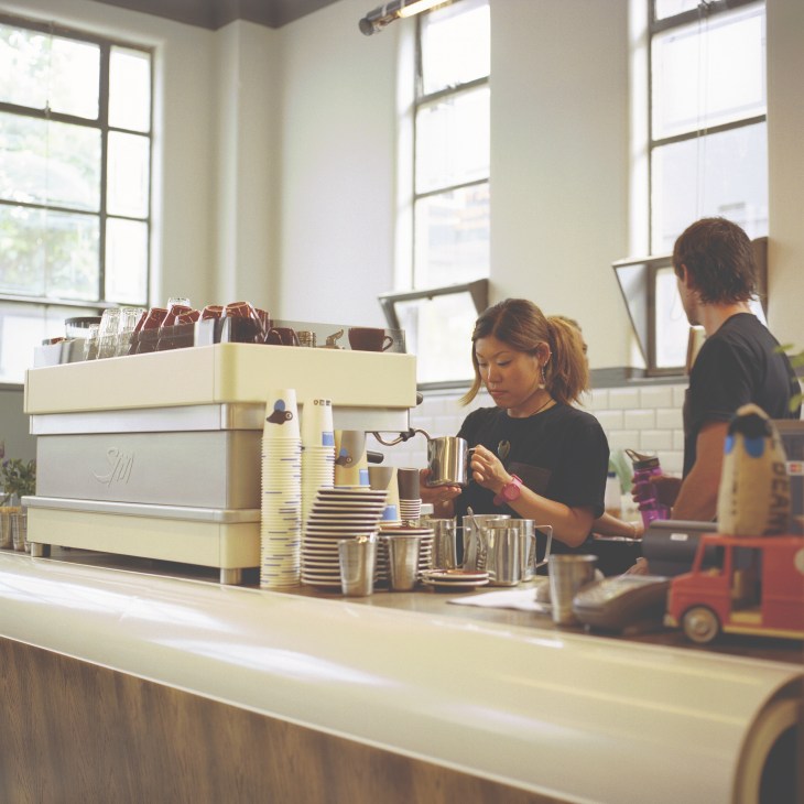 Barista preparing coffee at Kokako café counter in Auckland with cream-coloured espresso machine.