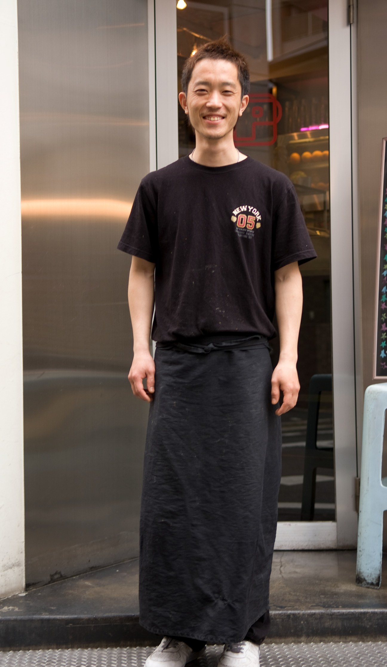 Koki Haramaki, a cook at Paloma Grill restaurant in Fukuoka, standing outside wearing a black t-shirt and long skirt.