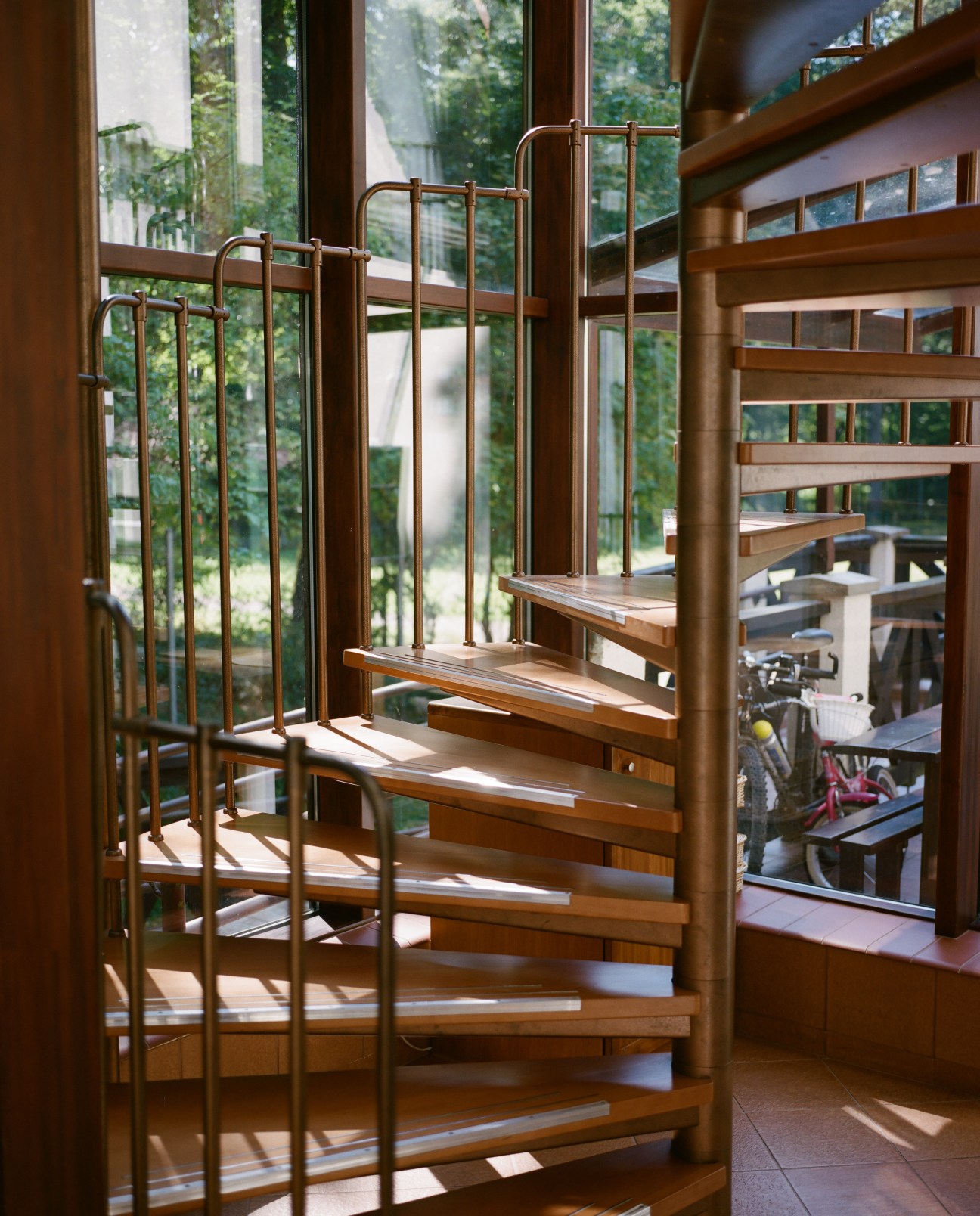 Wooden stairs with metal railings leading upward with forest views through large windows.