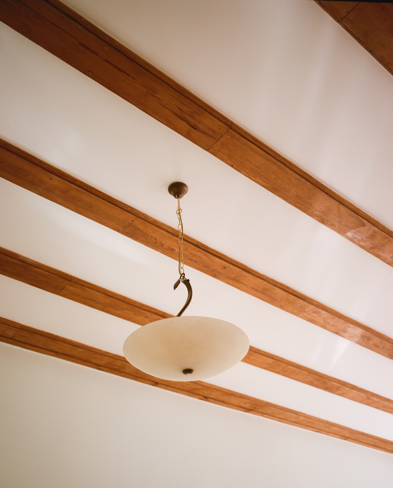 Pendant ceiling lamp hanging from wooden beam in white interior with original wooden beams.