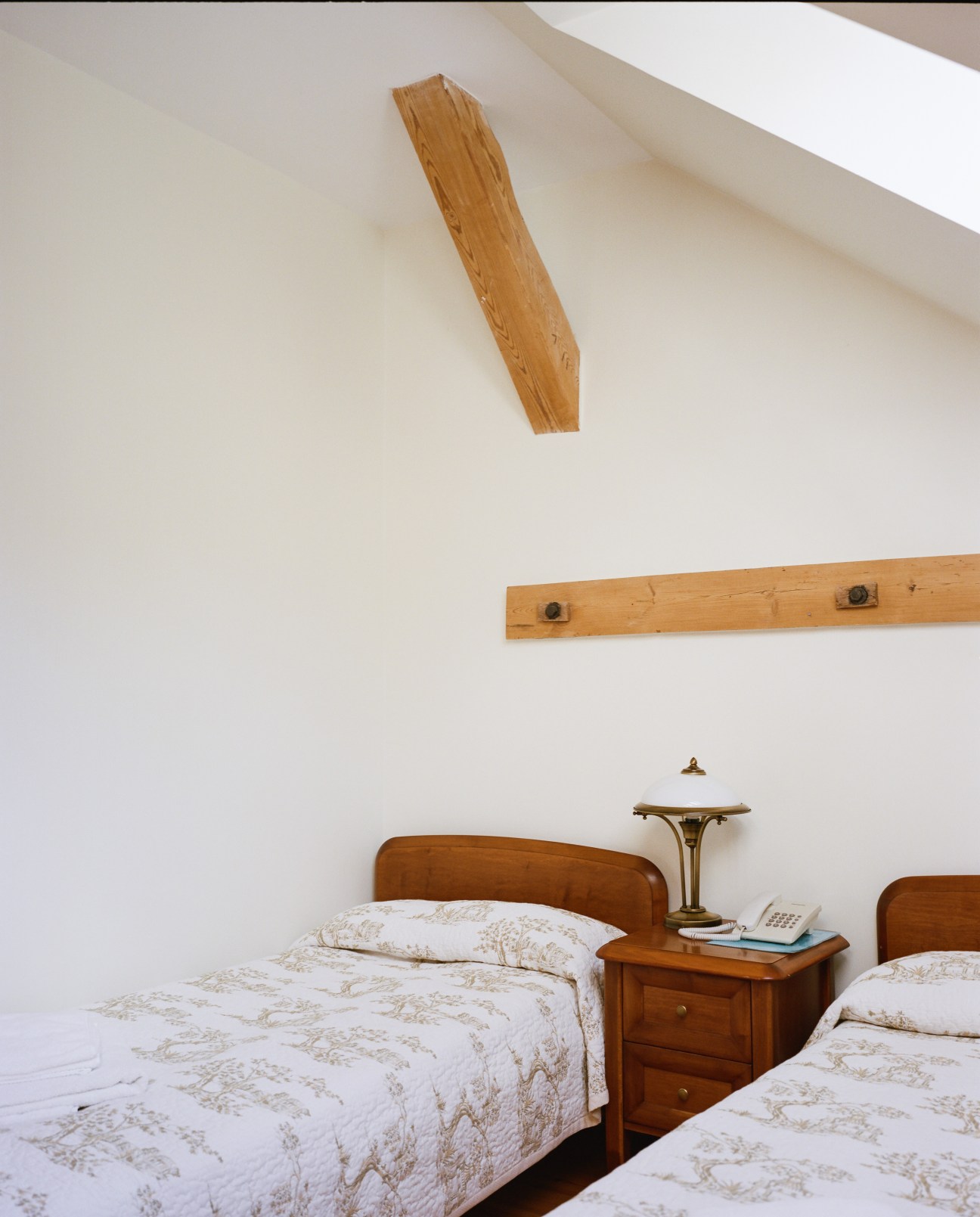 Twin bedroom at Nibork retreat with wooden beds, patterned bedding, and original wooden beams on white walls.