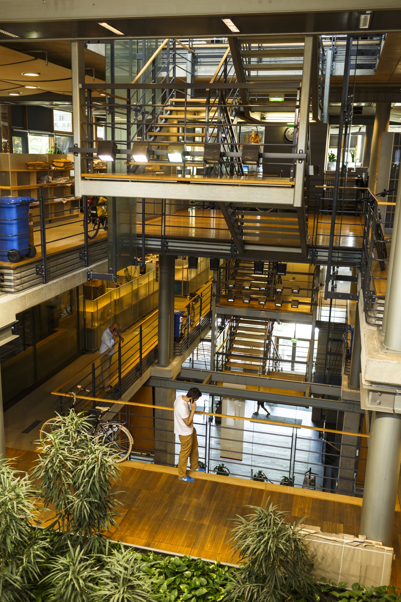 Multiple levels of Gazeta Wyborcza's office interior with wooden stairs, railings, and plants between floors.