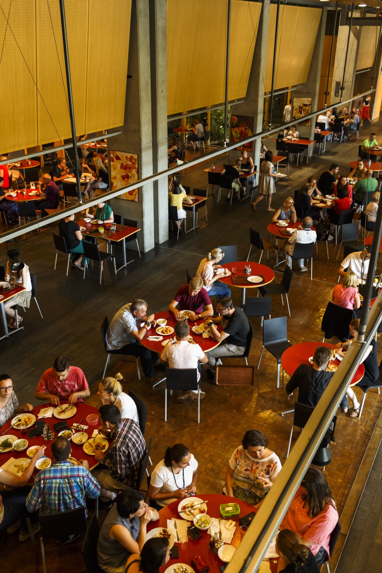 Overhead view of Gazeta Wyborcza's ground floor café with staff and visitors dining at red tables under yellow window shades.