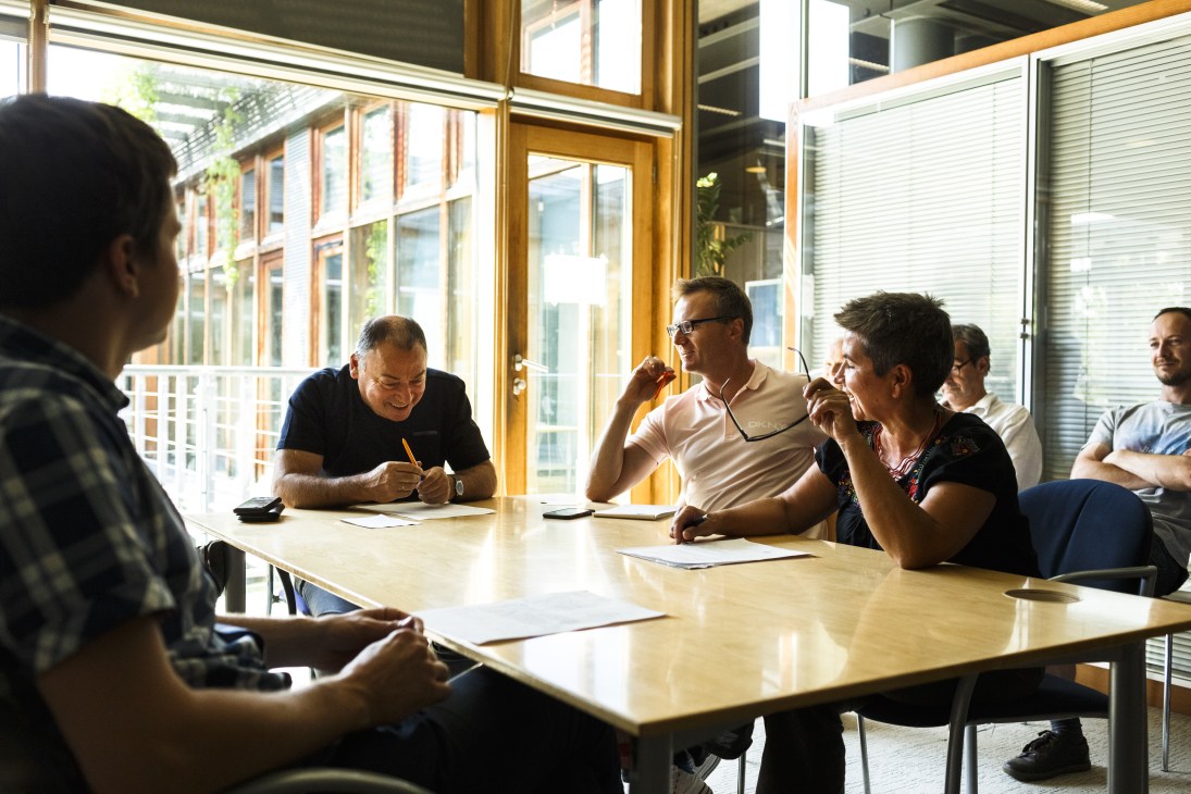 Gazeta Wyborcza journalists in discussion during an editorial meeting at a wooden table by large windows.