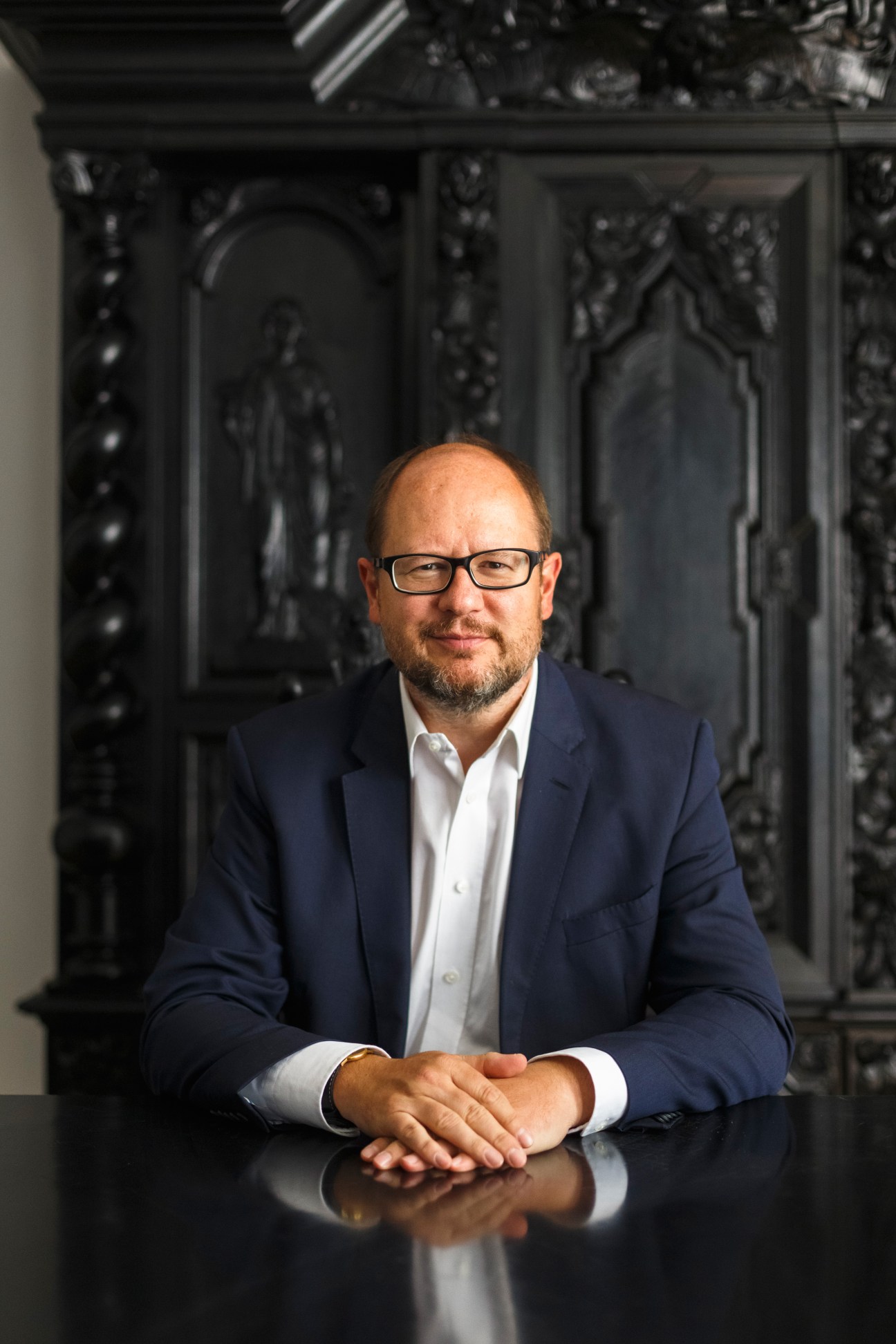 Mayor of Gdansk Pawel Adamowicz seated at a table wearing glasses and a dark blazer.