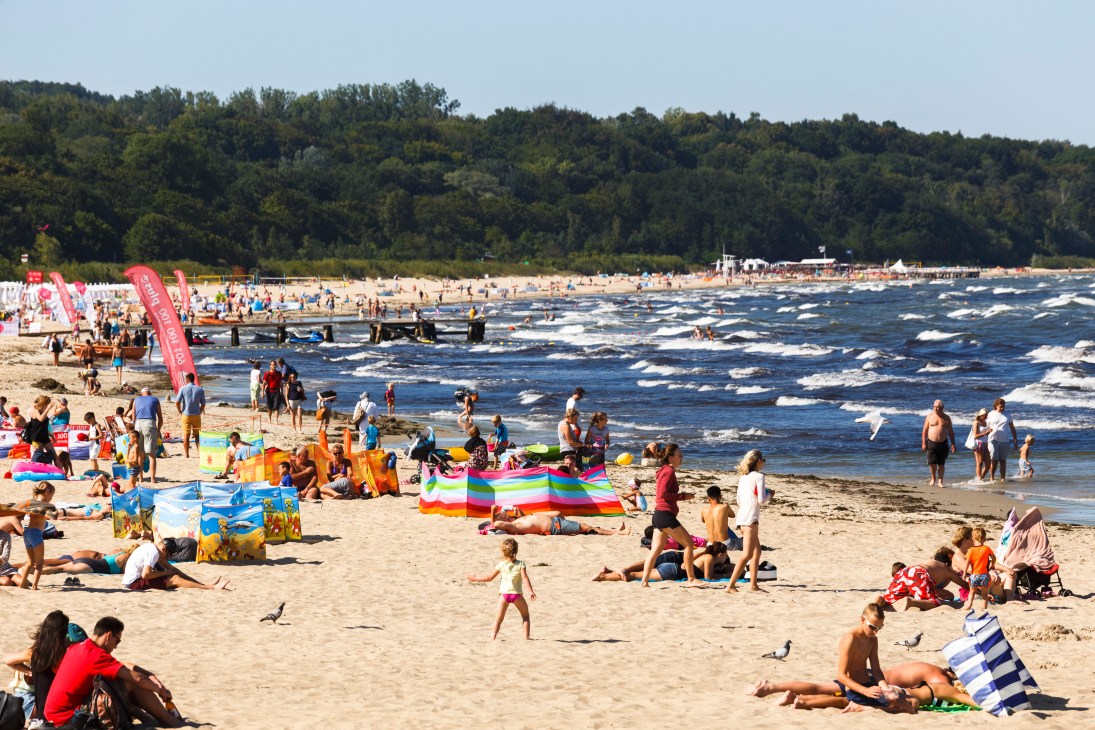 Crowded beach in Sopot with swimmers, sunbathers, and colorful beach equipment along the Baltic Sea.