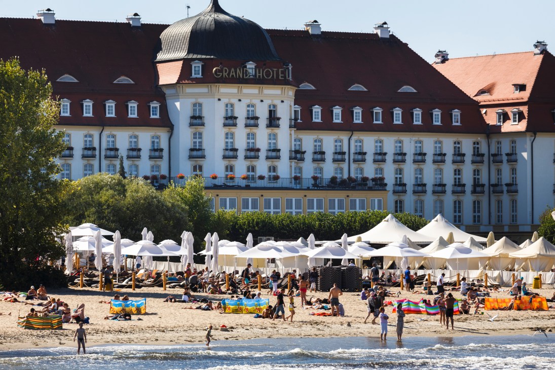 Grand Hotel in Sopot overlooks a crowded beach with white umbrellas and sunbathers on the Baltic coast.