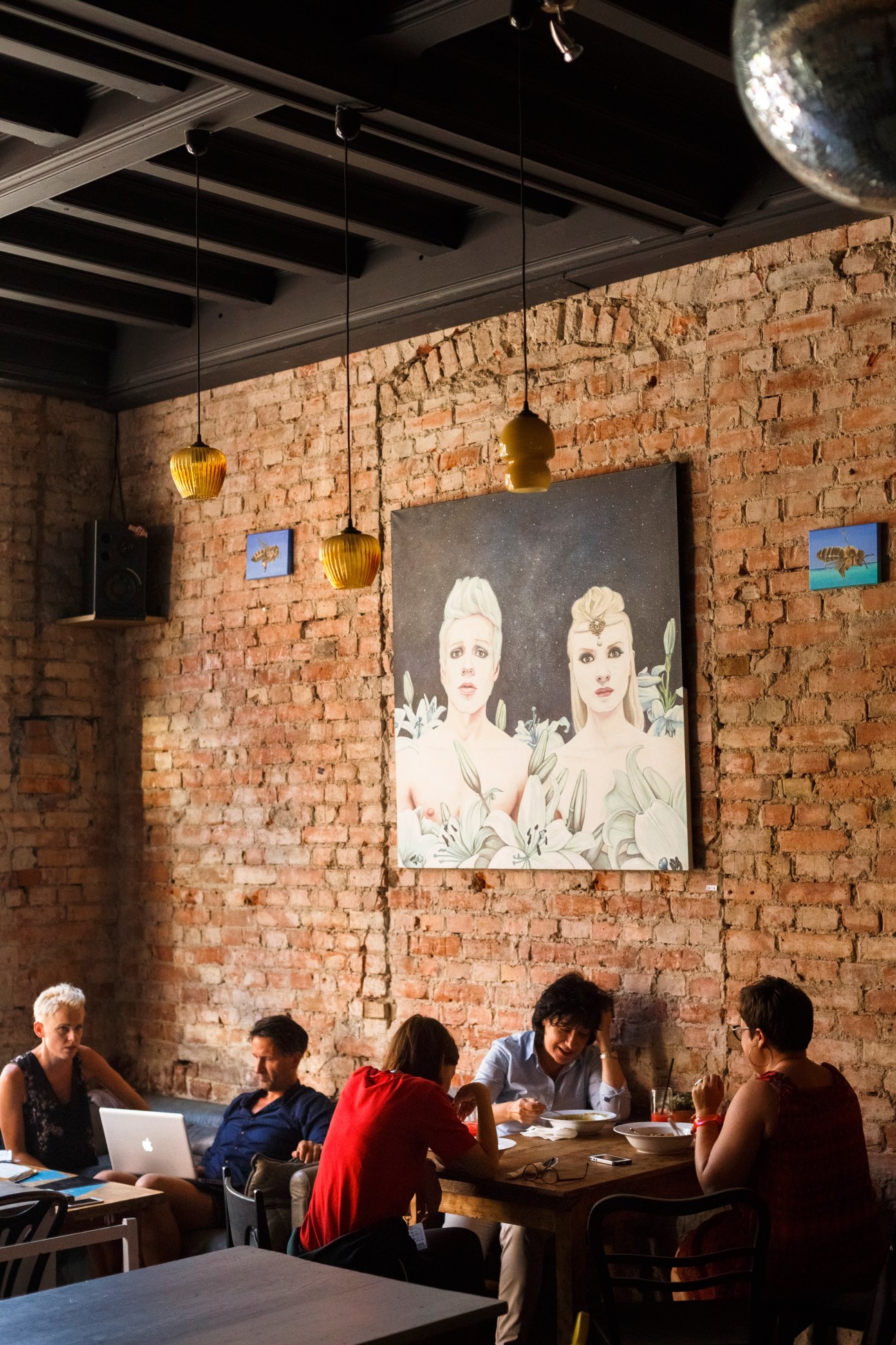 Dwie Zmiany café in Sopot with exposed brick walls, hanging brass pendant lights, and patrons seated at wooden tables.