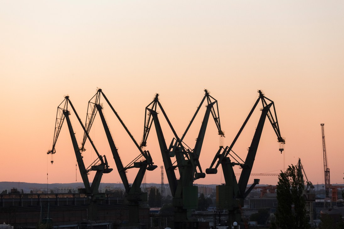 Silhouettes of industrial cranes at Gdansk shipyard against a pink sunset sky.